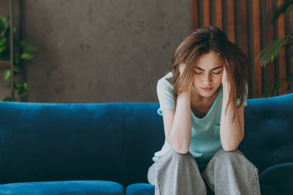Young bohemian woman with depression holding head while sitting on couch.