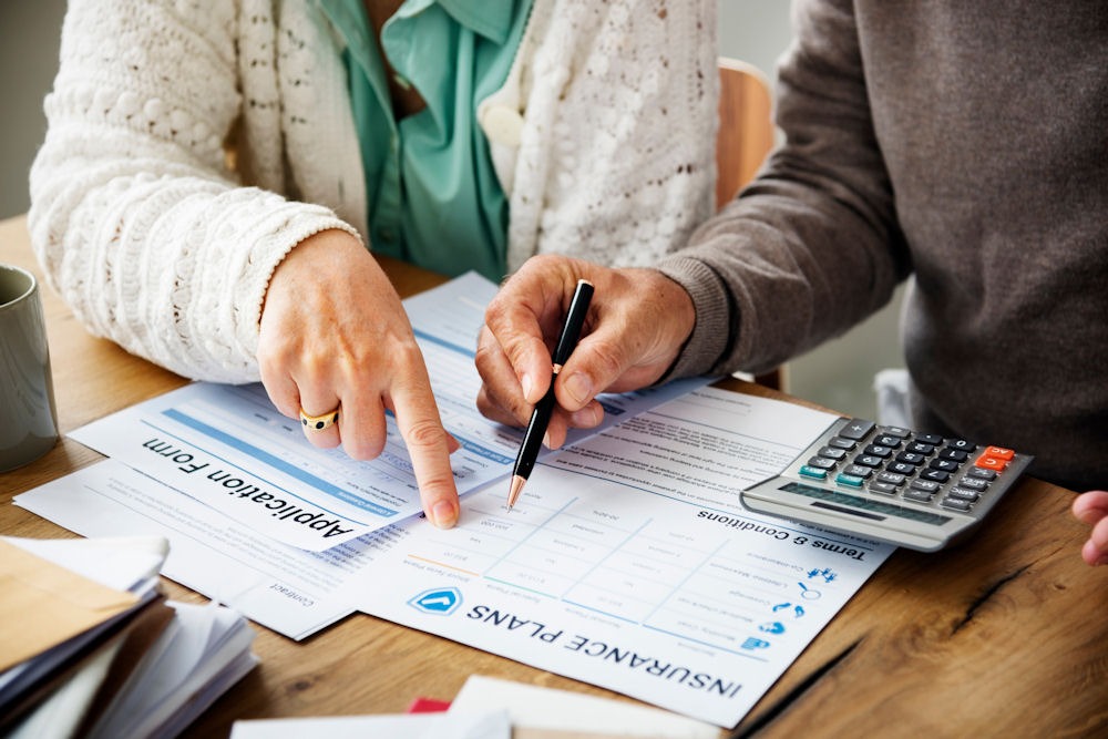 Couple reviewing insurance plans for rehab coverage with application forms and calculator on the table