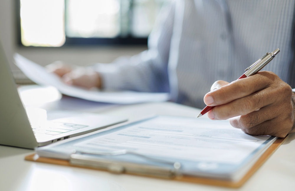 Man filling out insurance forms for rehab programs using a clipboard and laptop