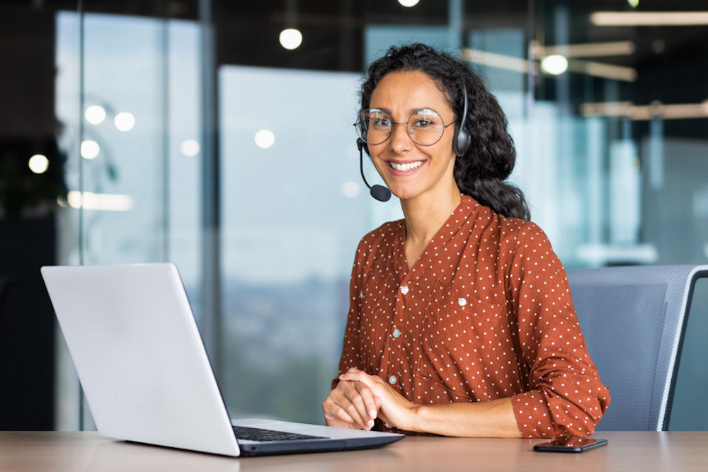 Lesbian woman smiling while working on laptop and wearing headset.