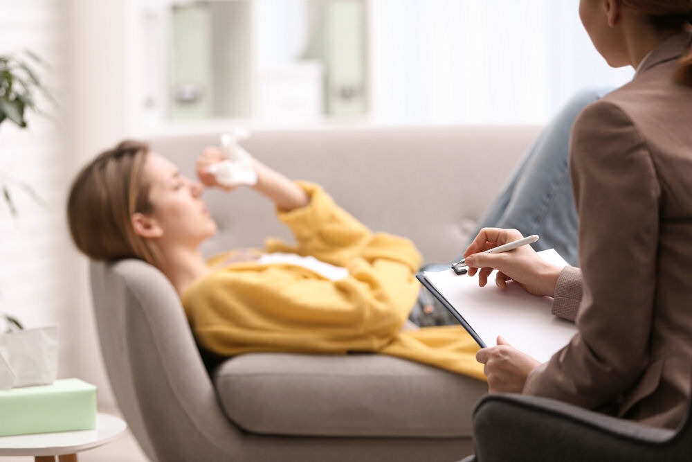 Veteran in yellow sweater lying down on couch talking to female therapist.
