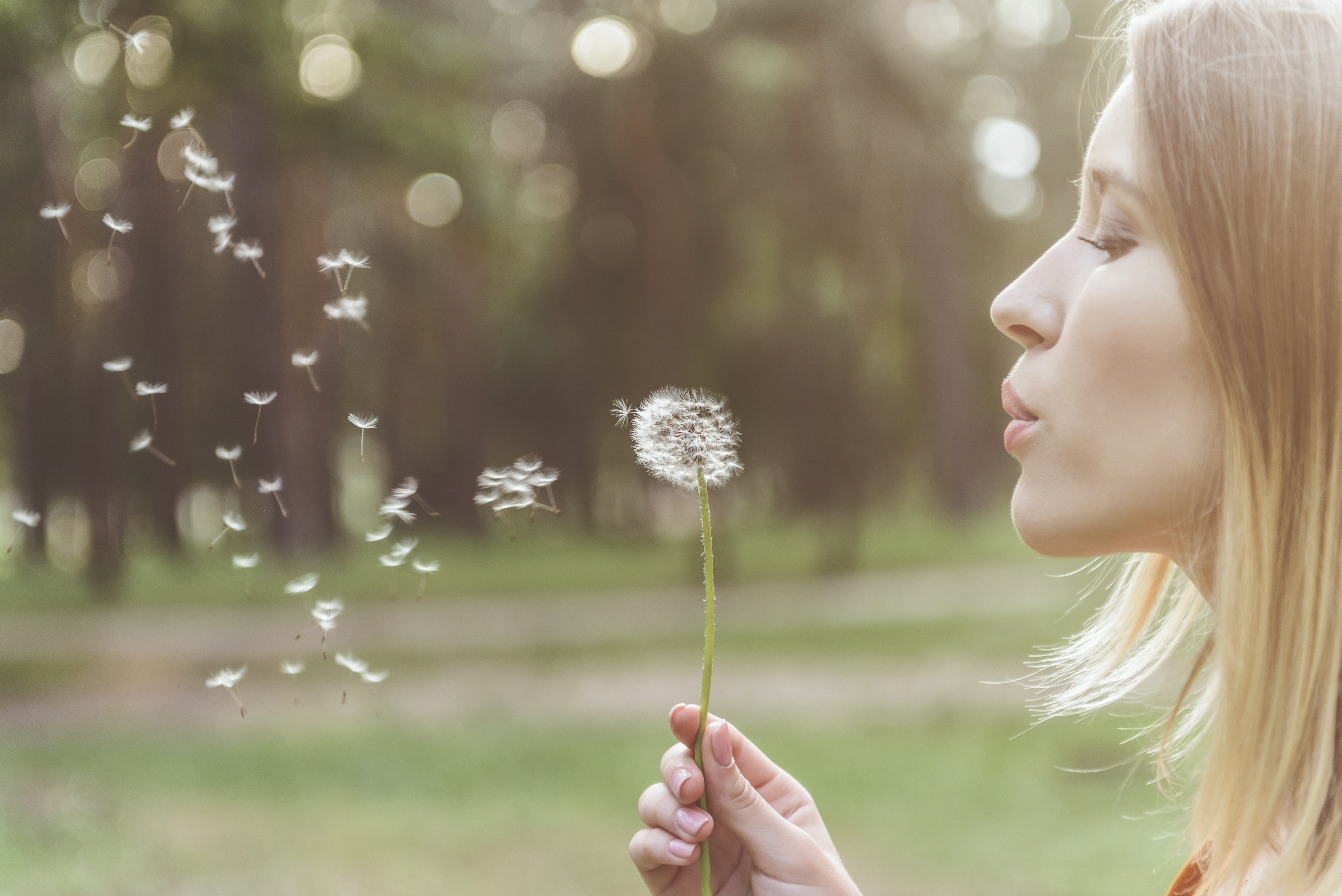 Woman with selective mutism bloeing air one a dandelion to practice calm breathing.