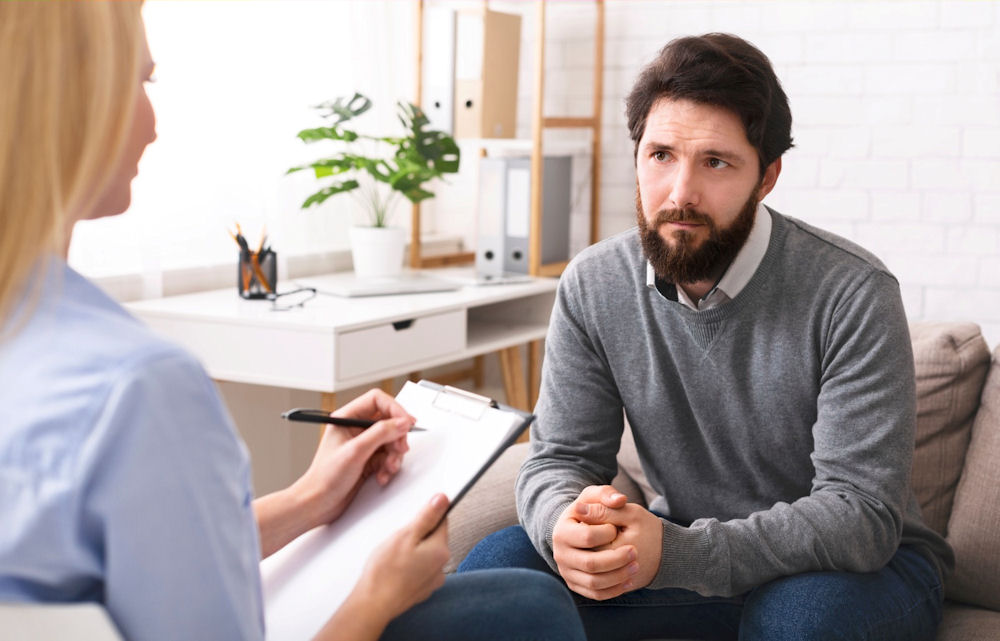 Male executive wearing sweater while speaking with therapist about addiction.